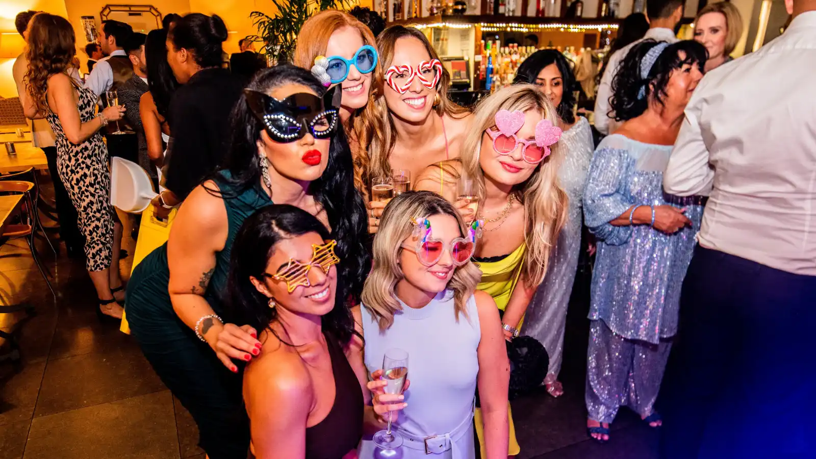 Bridal party posing with props in front of an open air photo booth backdrop